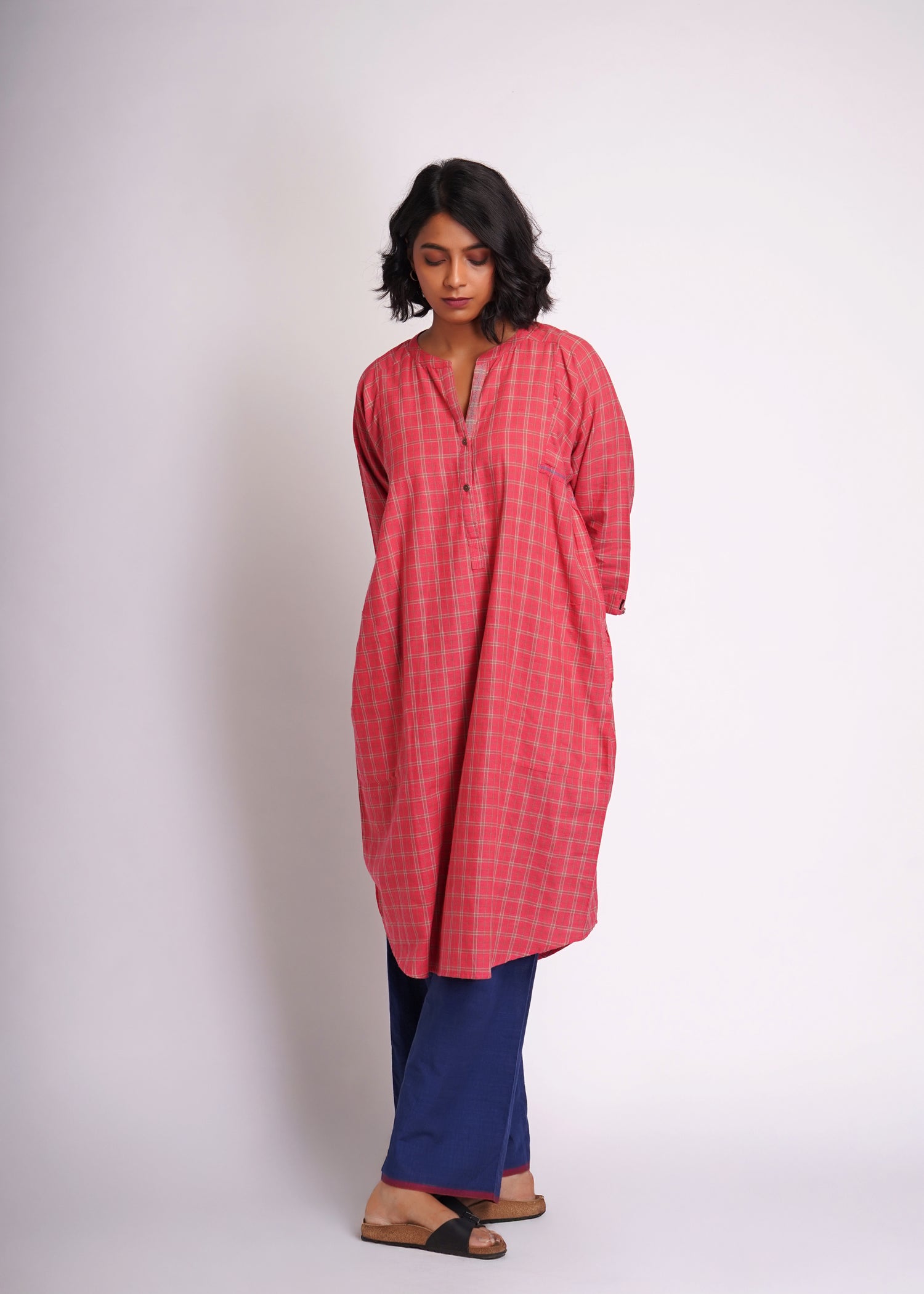 Woman wearing a red checkered kurta with blue pants on a white background