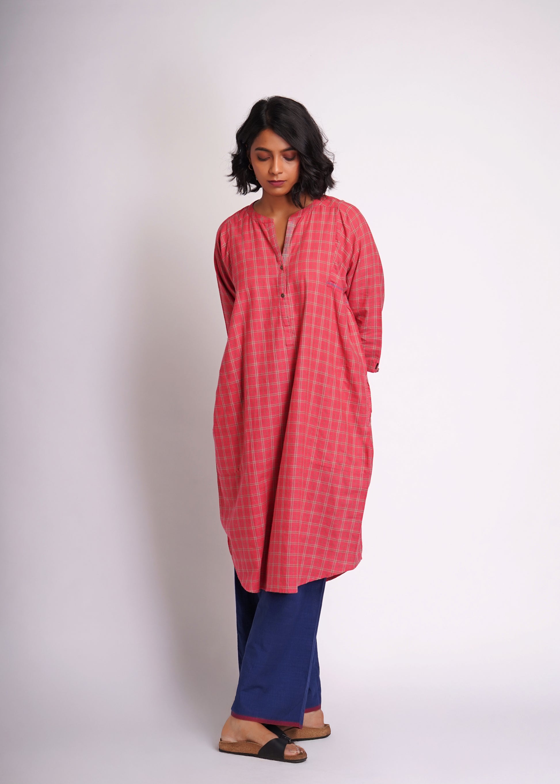 Woman wearing a red checkered kurta with blue pants on a white background
